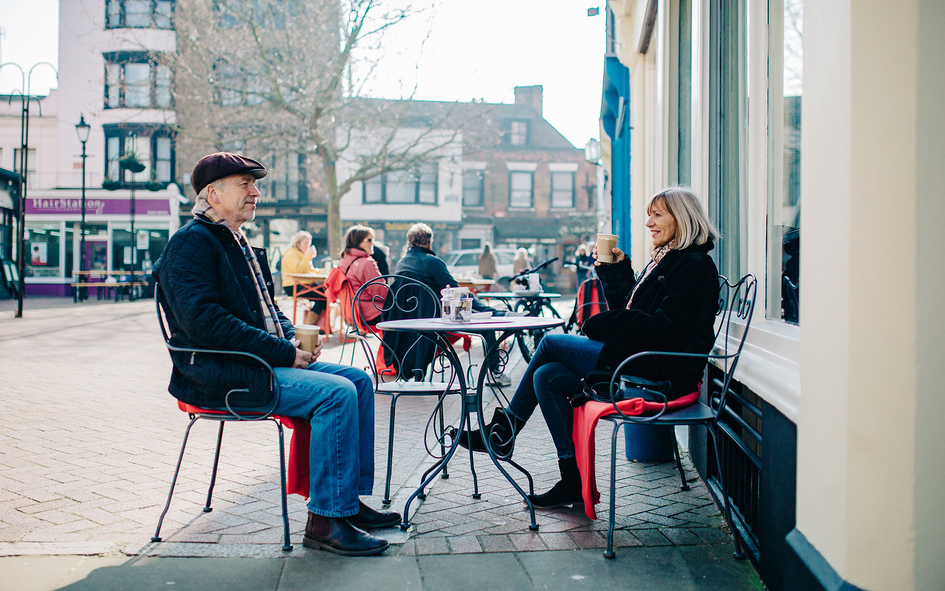 A couple holding coffee cups, sitting at an outdoor cafe table in Margate's Old Town.