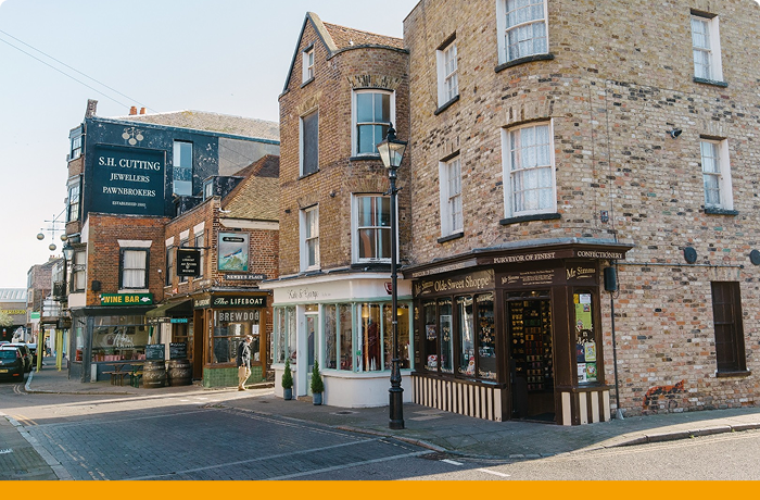 Row of brick shop fronts onto road with orange stripe at bottom of image