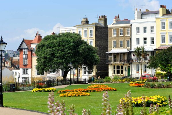 Park, garden area with buildings in background. Trees, lamp post and orange/yellow flowerbeds