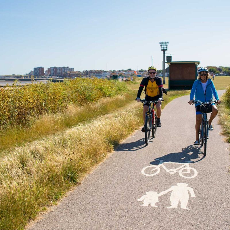 Lady and man cycling along path above beach
