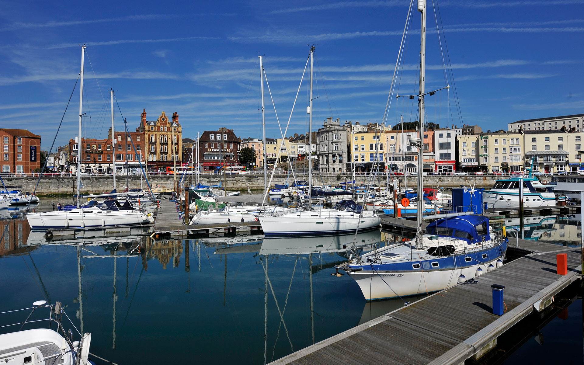 Yachts moored in Ramsgate harbour with sails down. Road and buildings in the background