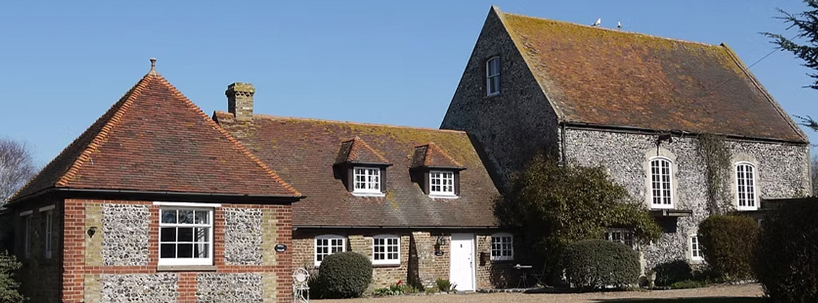 Three linked flint cottages with gravelled pathing and bushes at front