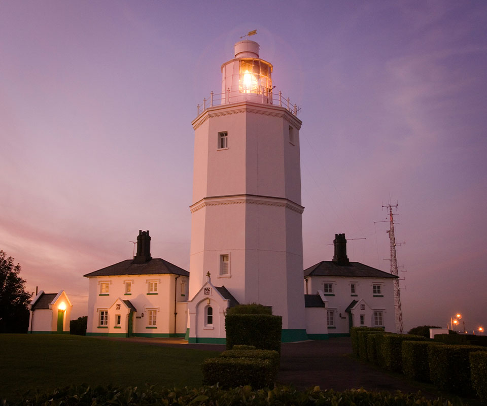 White lighthouse lit at dusk with white cottage either side