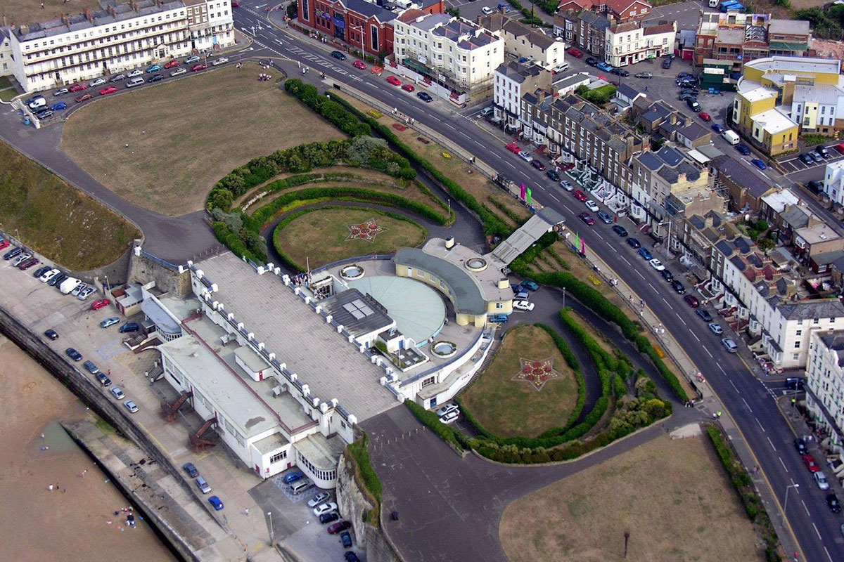 Aerial view of entertainment venue built into cliffs, gardens either side and promenade in front
