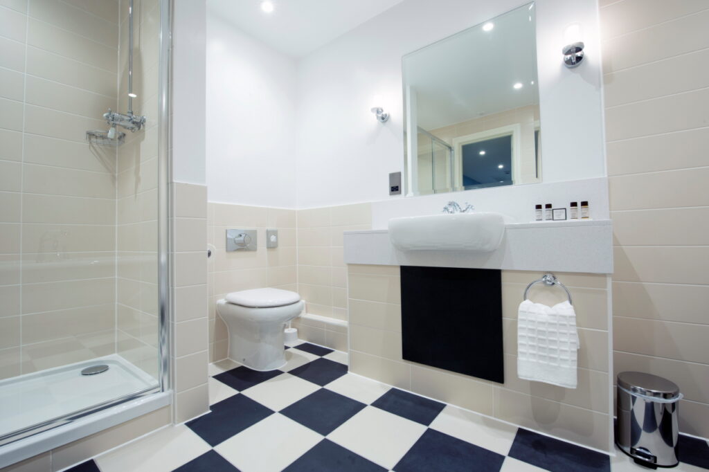 Large white and cream bathroom with shower unit, toilet and sink with mirror. Blue and white floor tiles