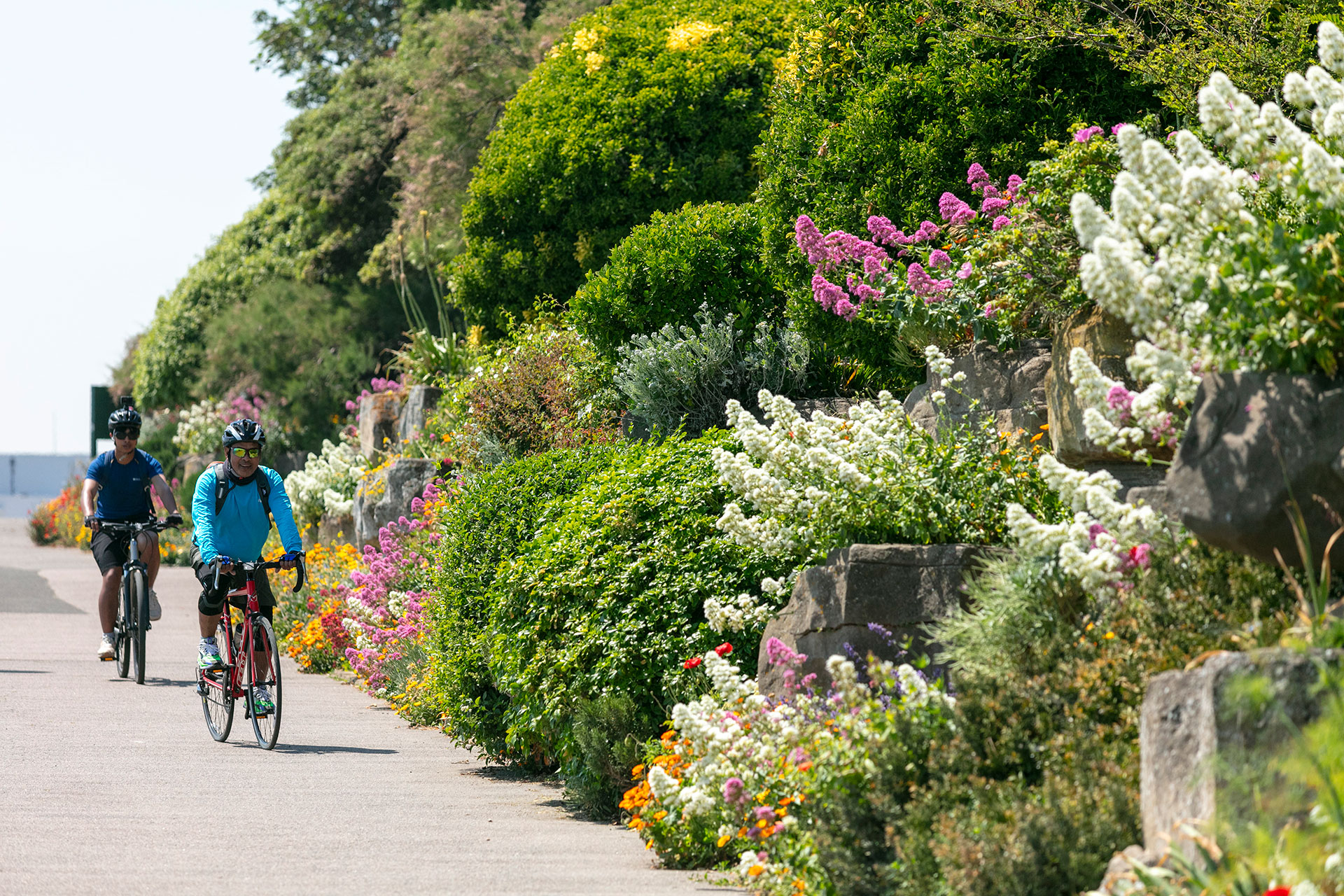 Cyclists riding past colorful flower gardens along a coastal path in Ramsgate.