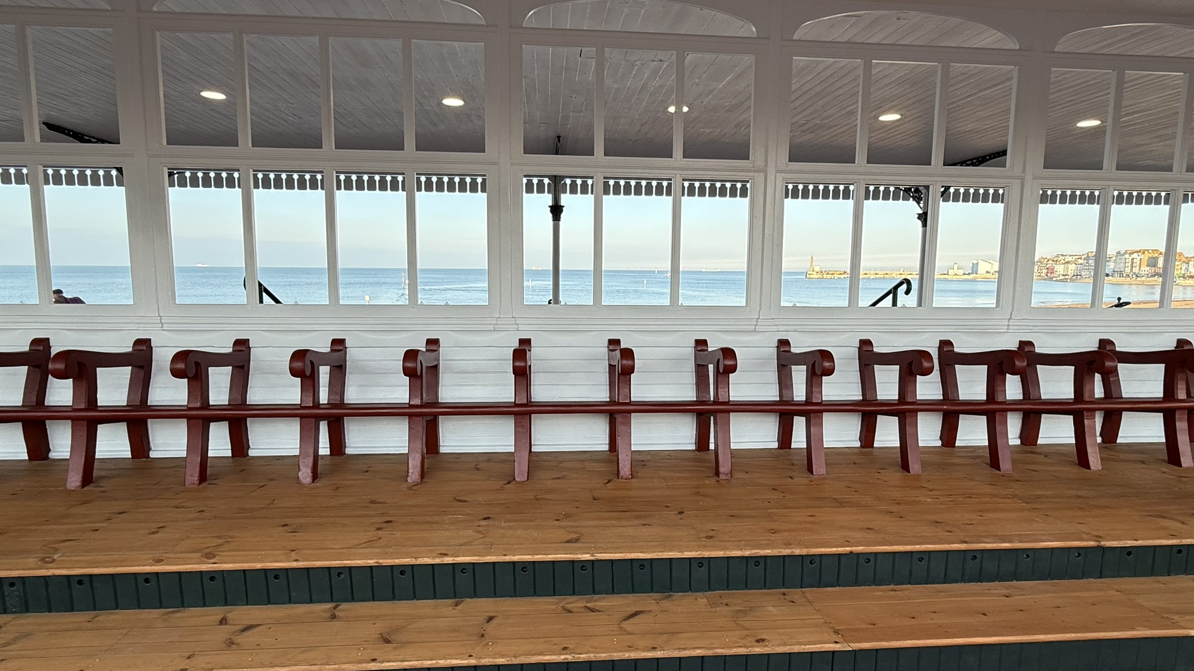 wooden bench seating in seaside shelter, looking to beach through windows