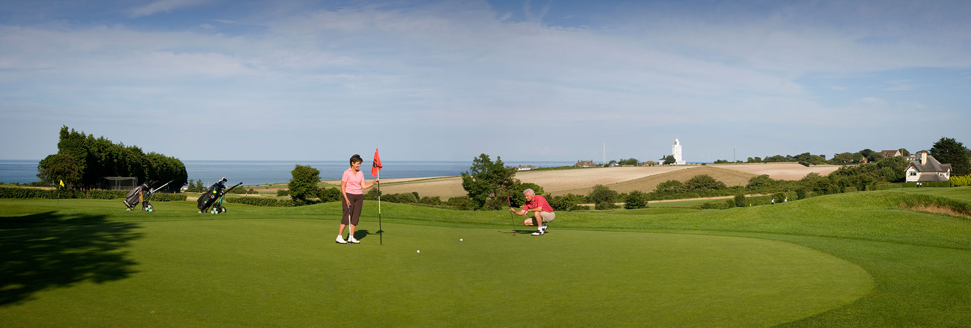 Golfers on the green at North Foreland Golf Course with the sea and lighthouse in the background.