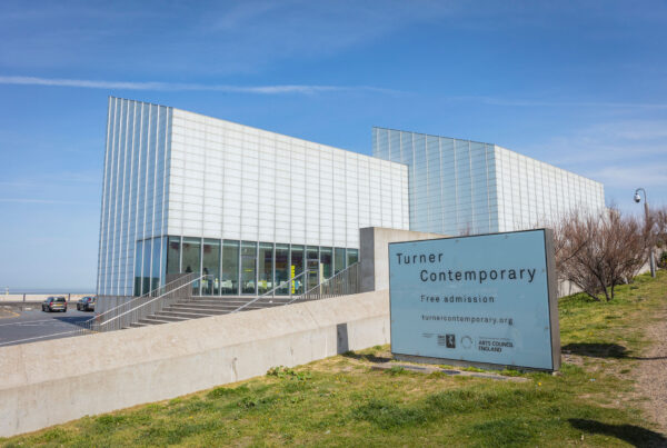 View to entrance steps and cafe of art gallery shaped like two fins. Welcome sign on grass area in front of building