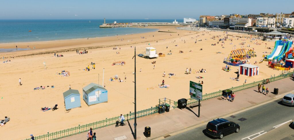 Aerial view of sandy beach with children's rides, tide out and looking across to harbour arm and Turner Contemporary
