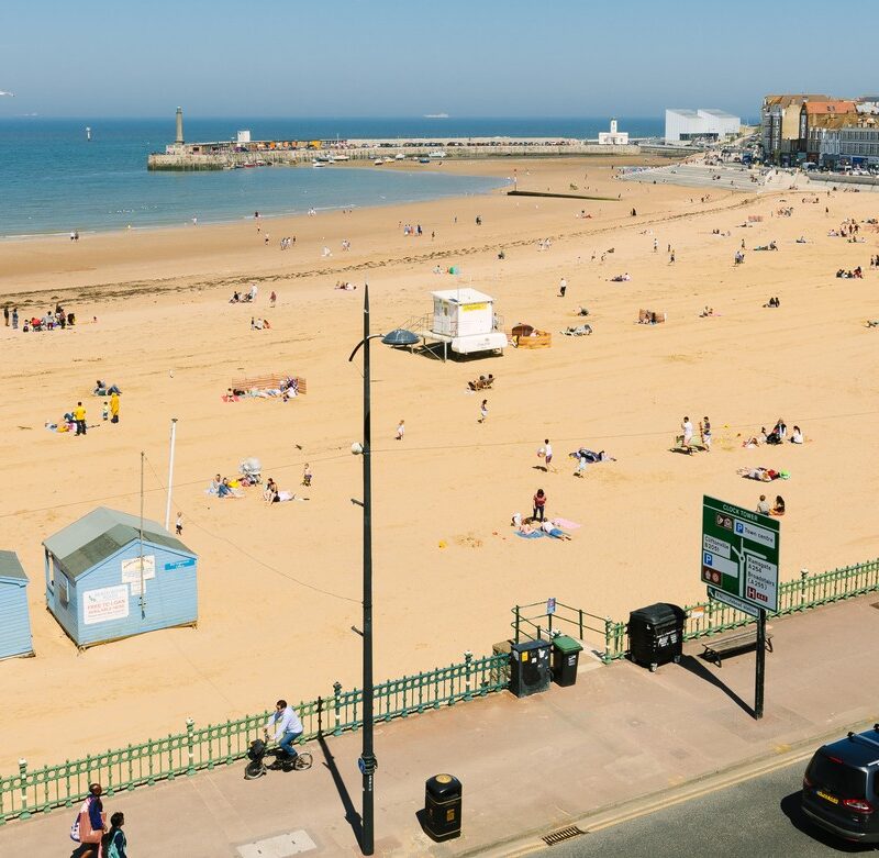 Aerial view of sandy beach with children's rides, tide out and looking across to harbour arm and Turner Contemporary